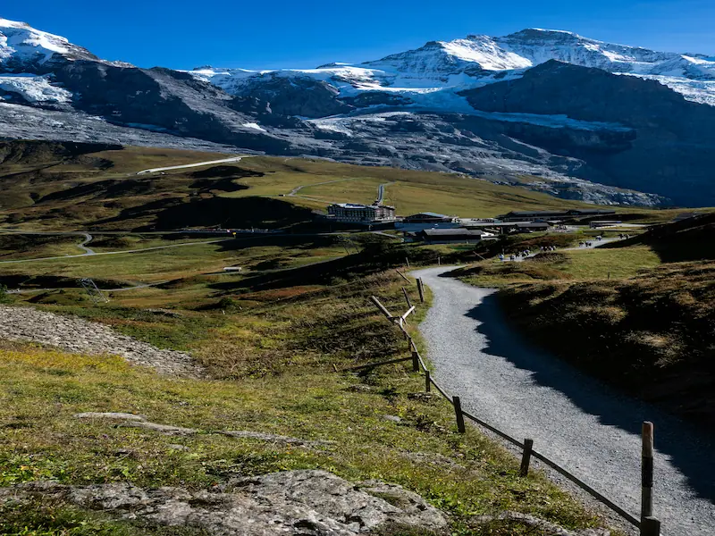 Hiking trail leading toward snow-capped mountain peaks near a mountain hotel in the Swiss Alps