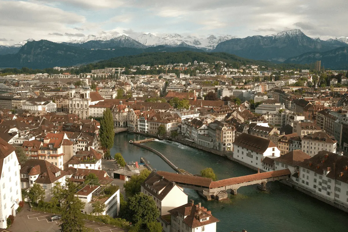 Aerial view of Lucerne's old town with the Reuss river, covered wooden bridge, and snow-capped Alps in the background