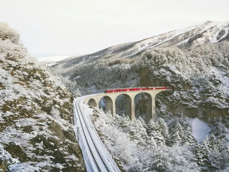 Red Rhaetian Railway train crossing a snow-covered stone viaduct in the Swiss Alps