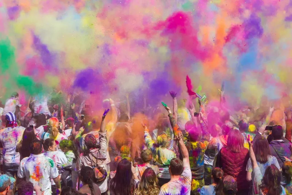 Crowd celebrating Holi festival with colored powder thrown into the air, India