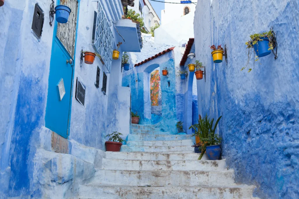 Narrow blue-painted alley with white stone steps and potted plants in Chefchaouen, Morocco's Blue City