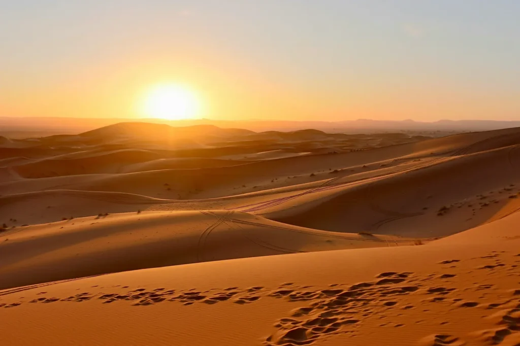 Sunrise over the golden dunes of the Sahara Desert near Merzouga, Morocco, with footprints in the sand