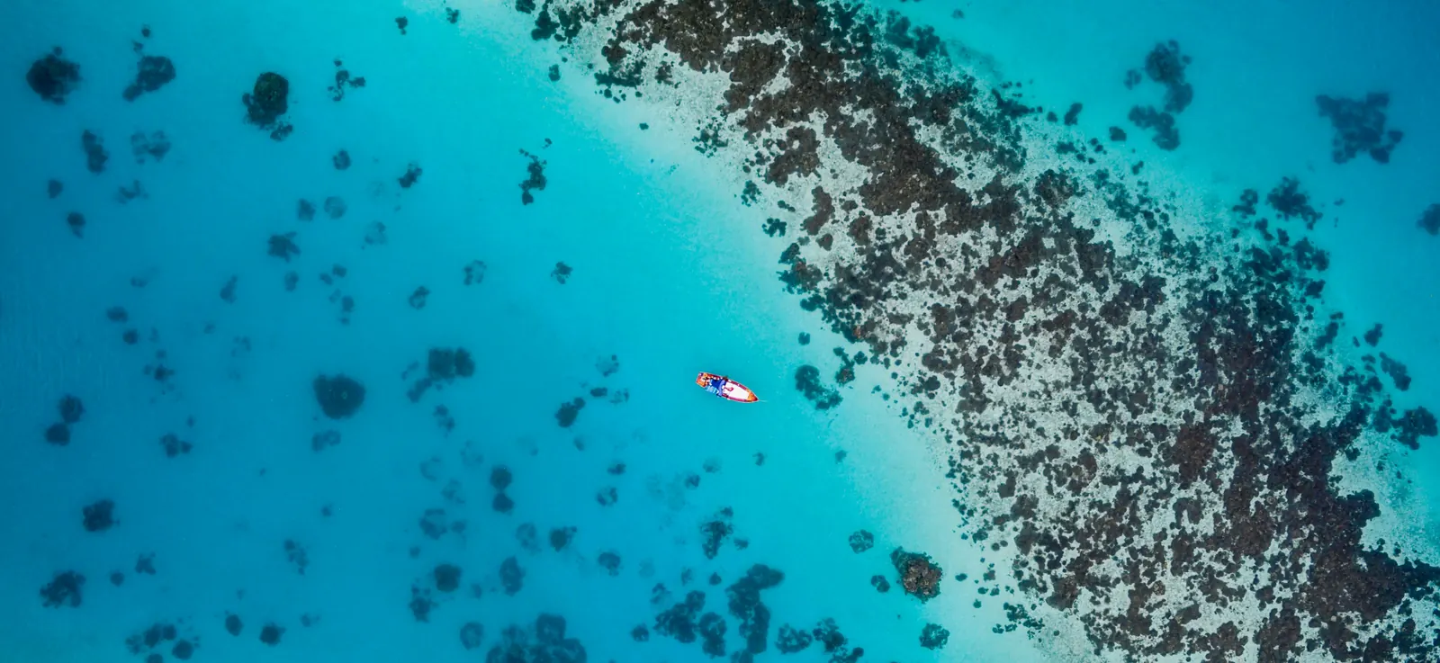 Aerial view of a small boat over coral heads in a turquoise Maldives lagoon