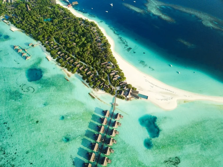Aerial view of a Maldives resort island with overwater villas and a white sand spit