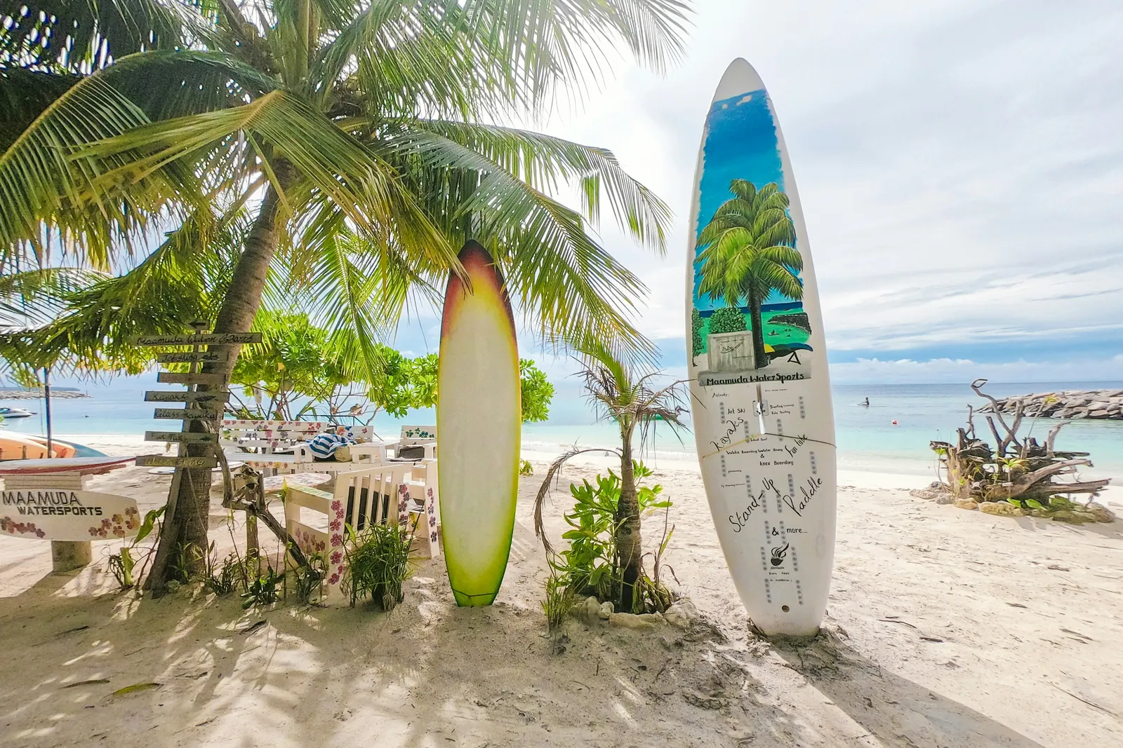 Two surfboards standing on a white sand beach beside a watersports sign in the Maldives