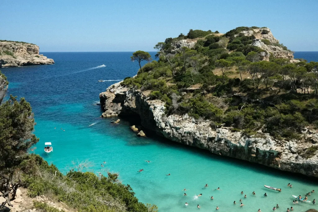 The turquoise water of Cala Turqueta cove in Mallorca, Spain, with swimmers and a boat