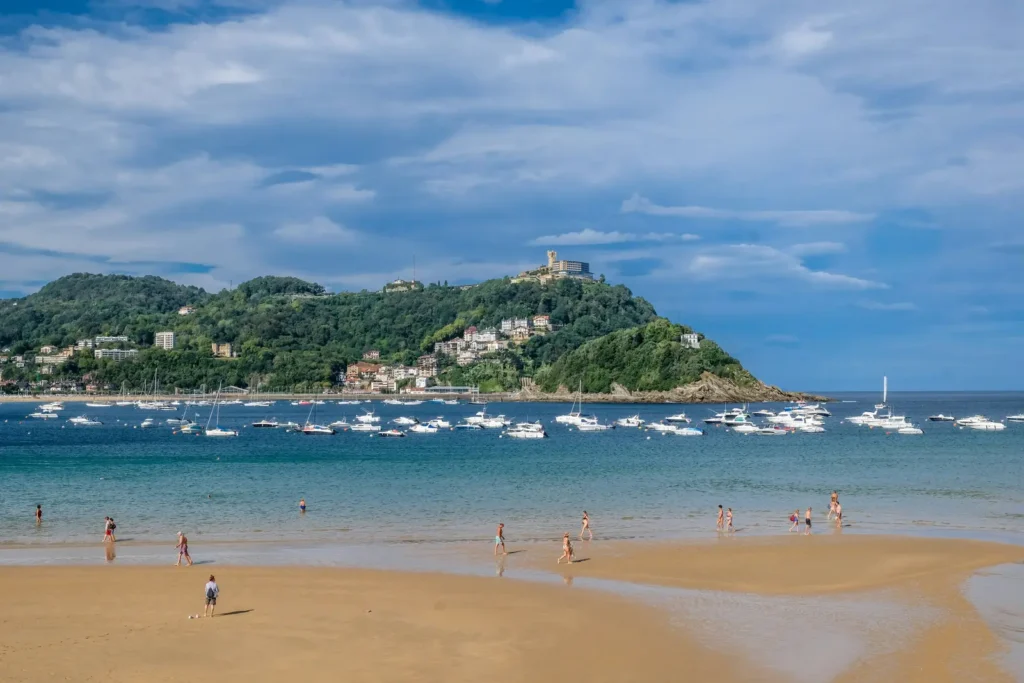 La Concha Bay in San Sebastián, Spain, with sailboats moored in the harbor and beachgoers on the sand