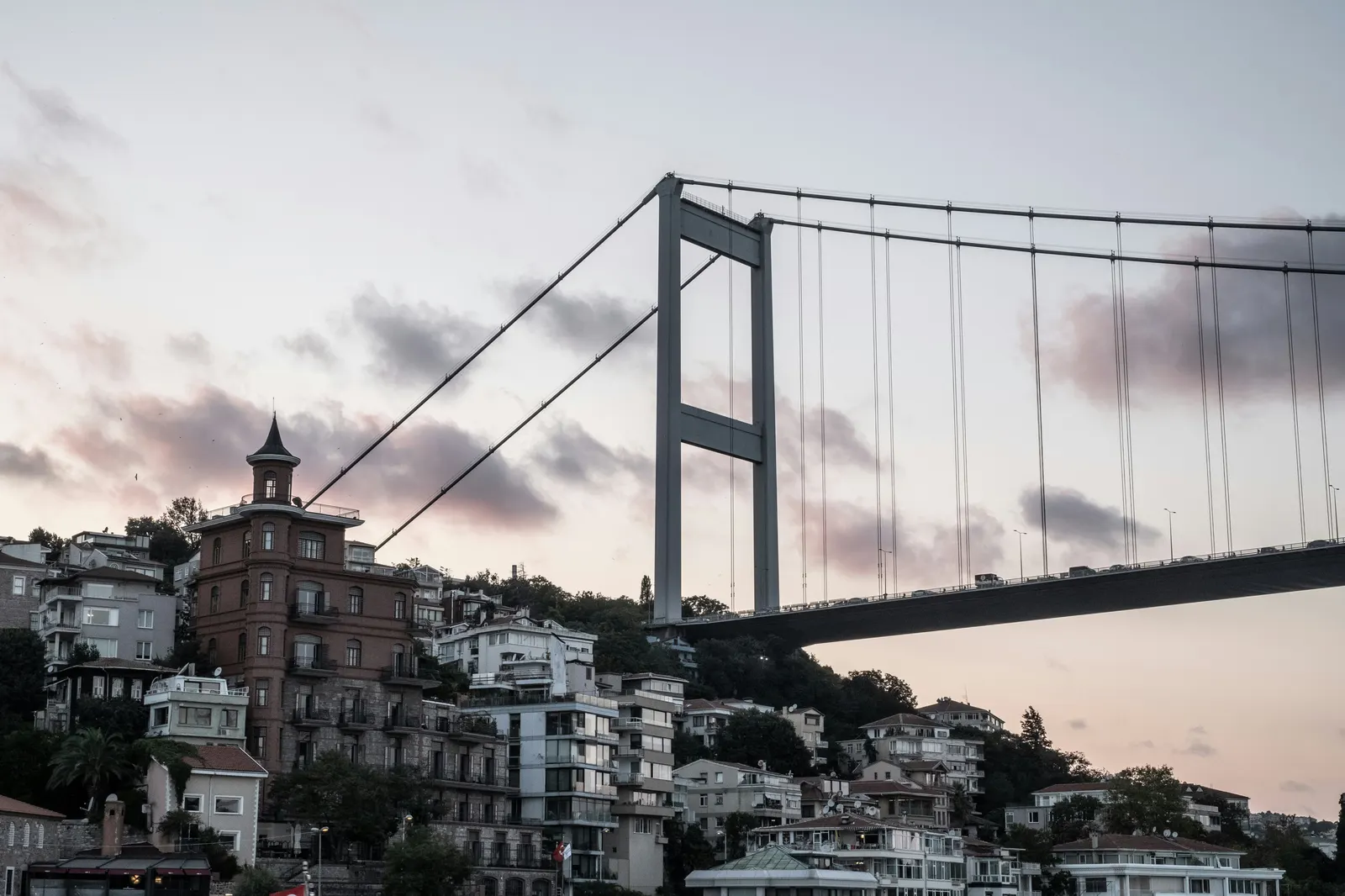 The Fatih Sultan Mehmet Bridge spanning the Bosphorus at dusk, with hillside apartments below