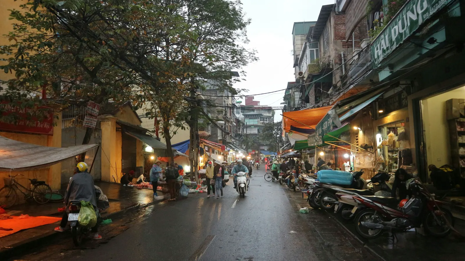 Motorbikes and street vendors on a rain-slicked street in Hanoi’s Old Quarter