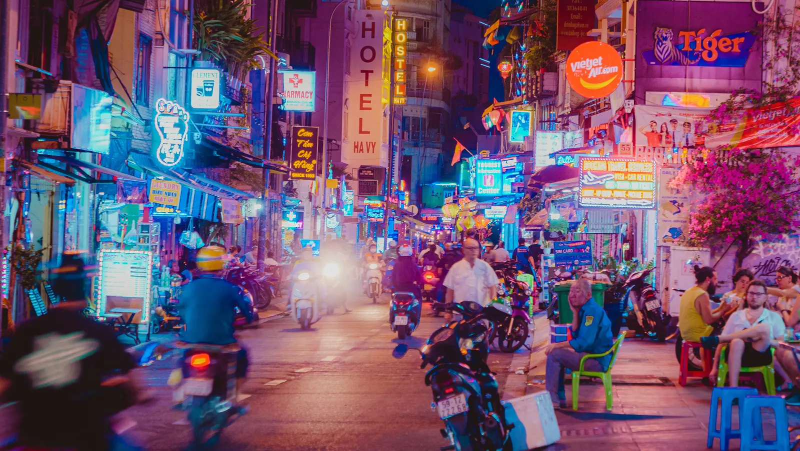 A busy, neon-lit street in Ho Chi Minh City at night with motorbikes and street vendors