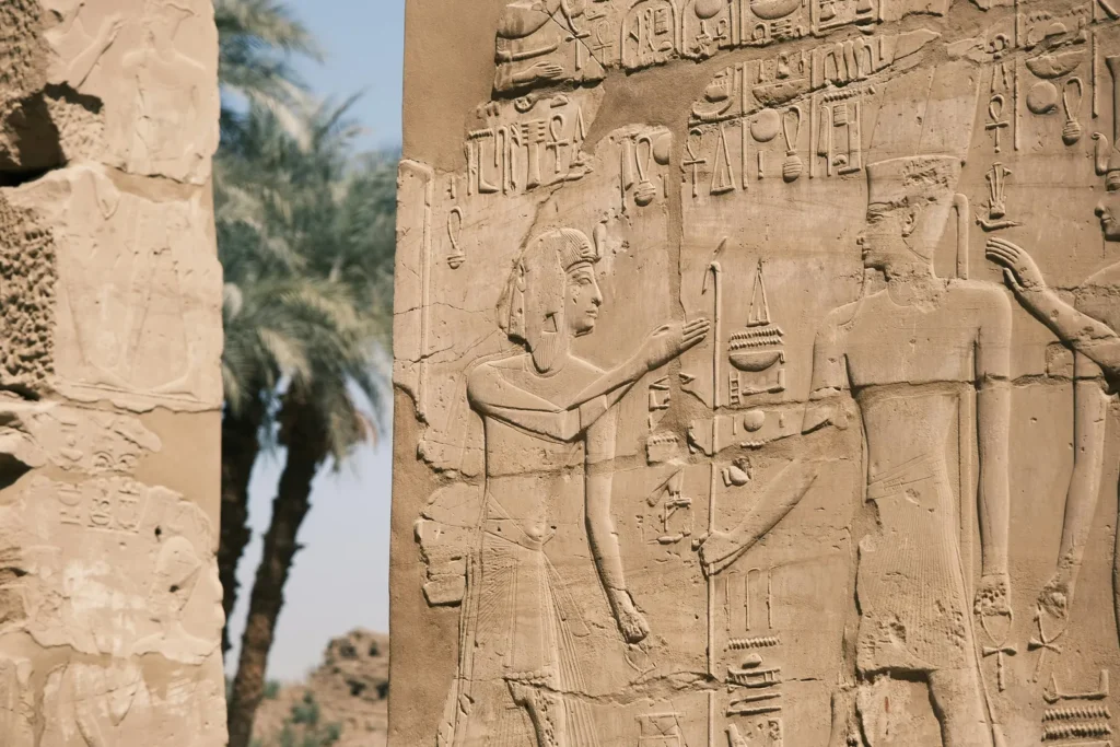 Carved relief of a pharaoh before a god at an ancient Egyptian temple beside date palms